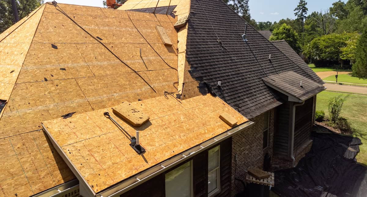 House with new roof being installed after hail damage. Roof decking exposed on half of the roof