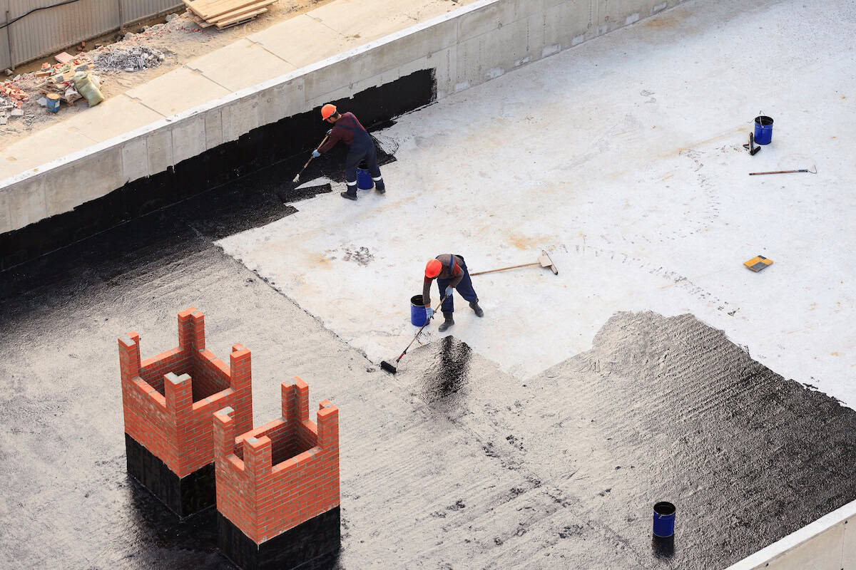Two workers conduct waterproofing of the roof with bitumen.