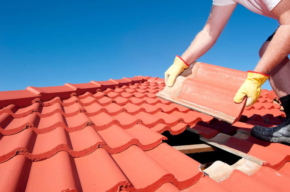 A roofer places large tile on roof of house
