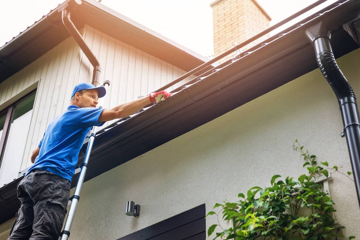 Man in blue uniform installing gutter system on house