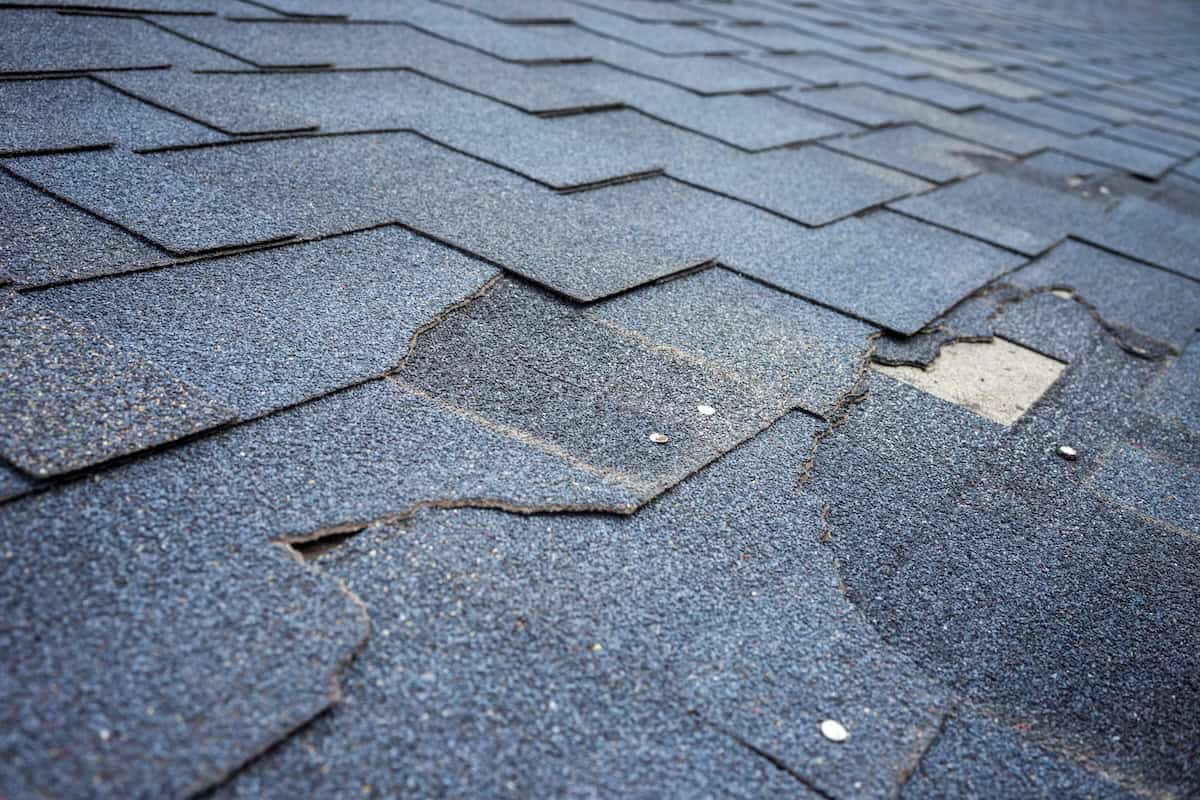 Сlose up view of bitumen shingles roof damage that needs repair.