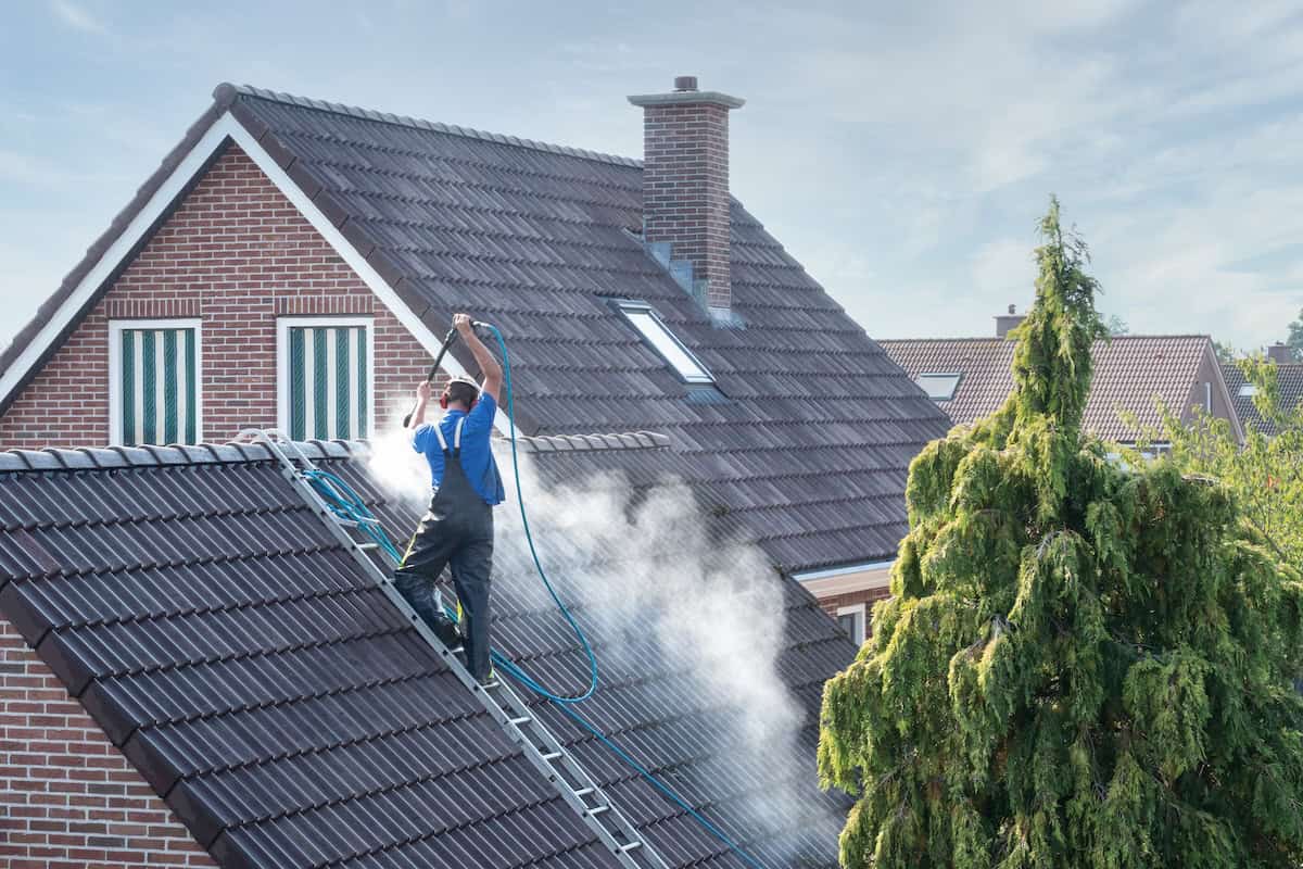 Cleaner with pressure washer at roof of house cleaning the roof tiles, removing moss and weeds