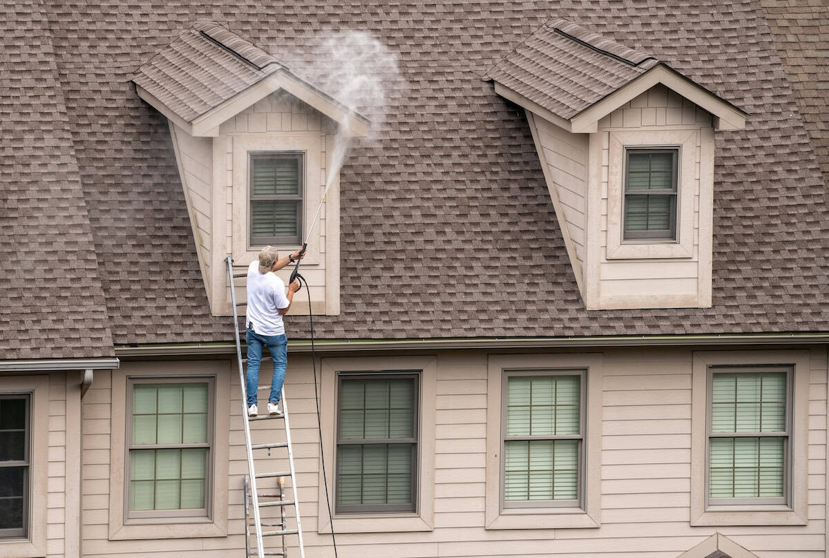 Painter on ladder using pressure wash spray to clean roof