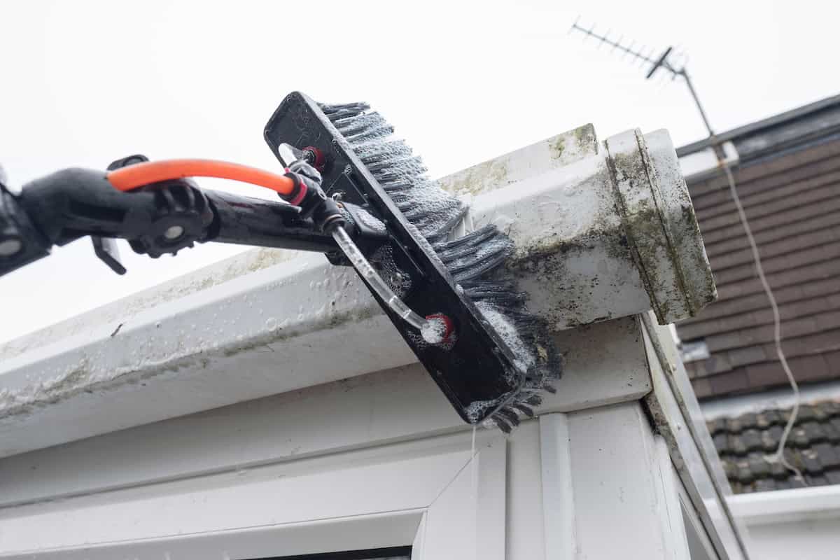A brush cleaning dirty clogged white plastic pvc gutters 