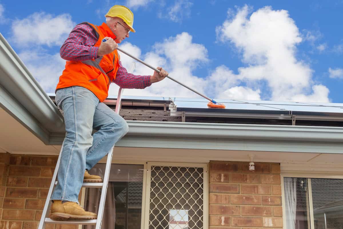 experienced worker cleaning solar panels on house roof