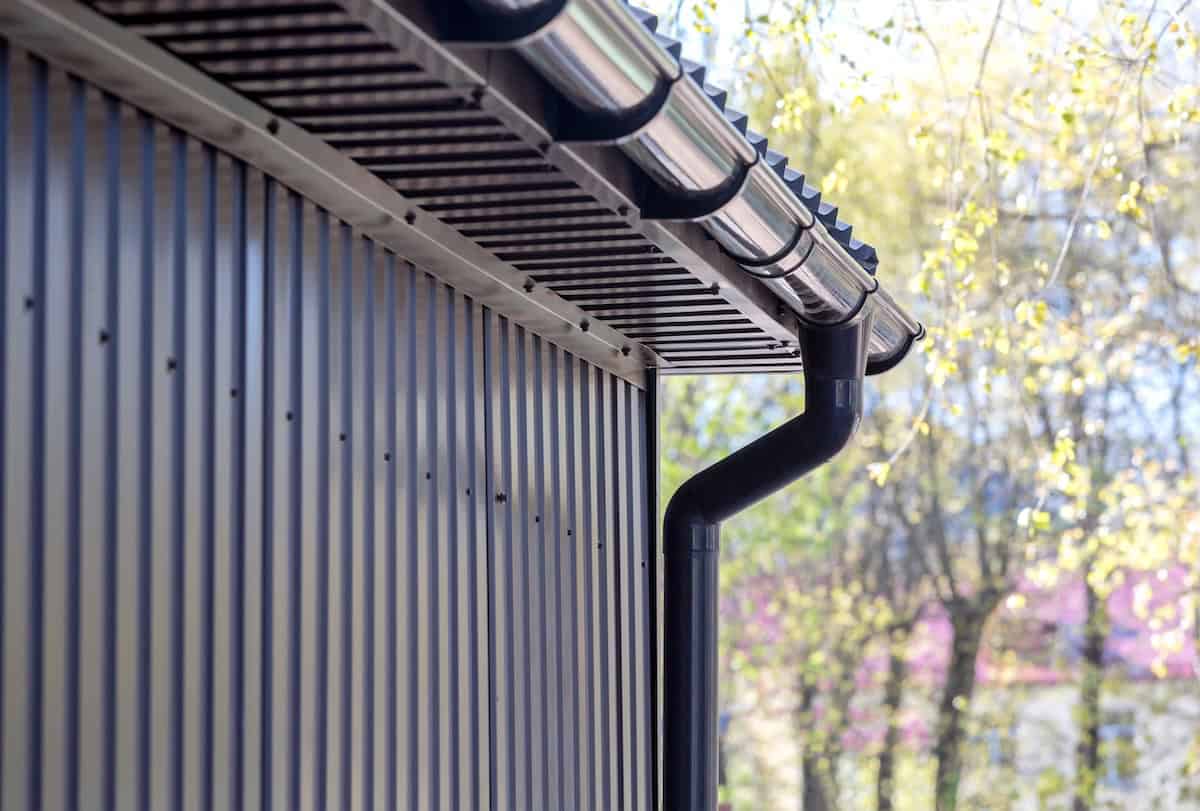 brown siding wall with plastic rain gutter and drainpipe
