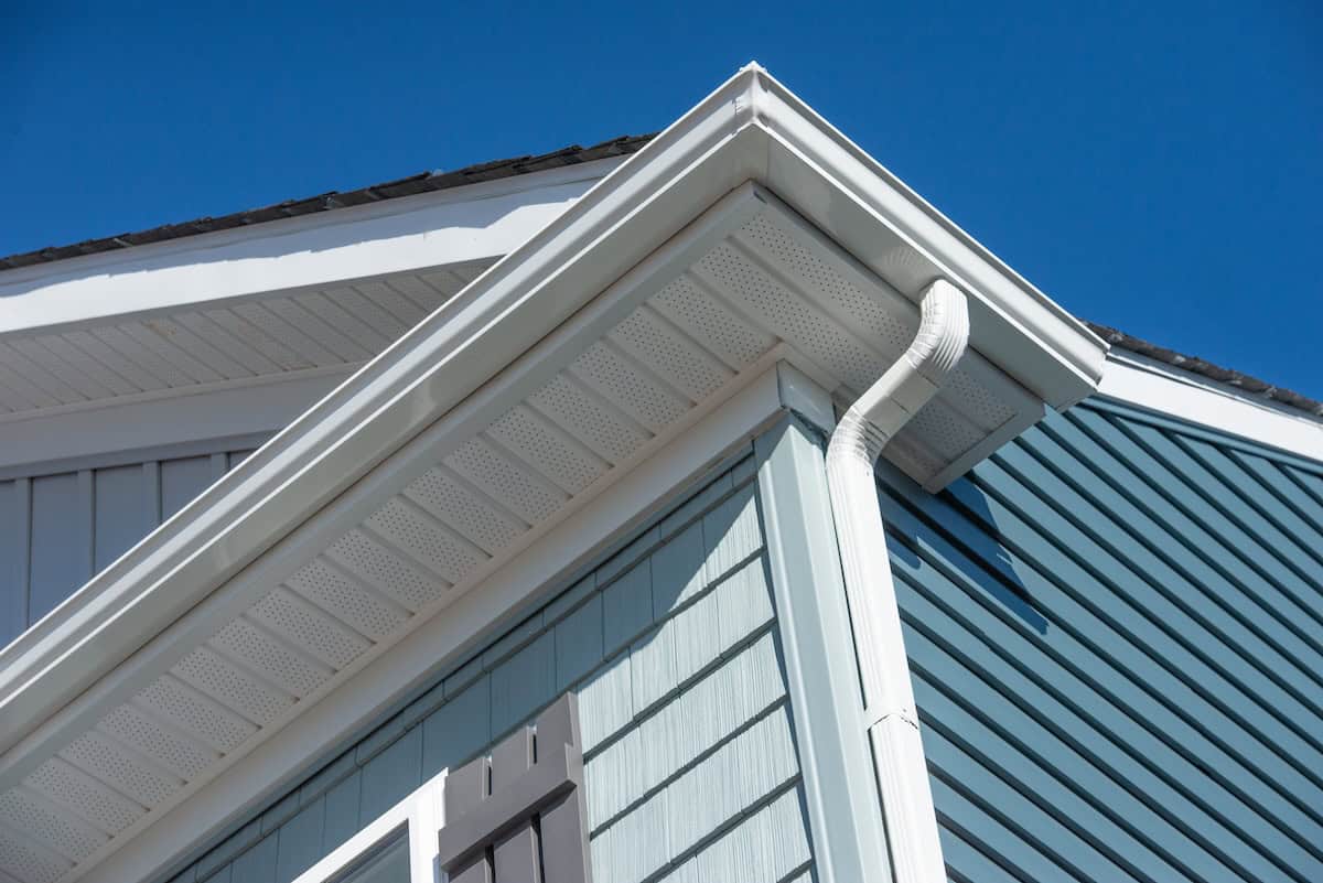 Colonial white gutter guard system, fascia, drip edge, soffit providing ventilation to the attic, with pacific blue vinyl horizontal siding at a luxury American single family home neighborhood USA