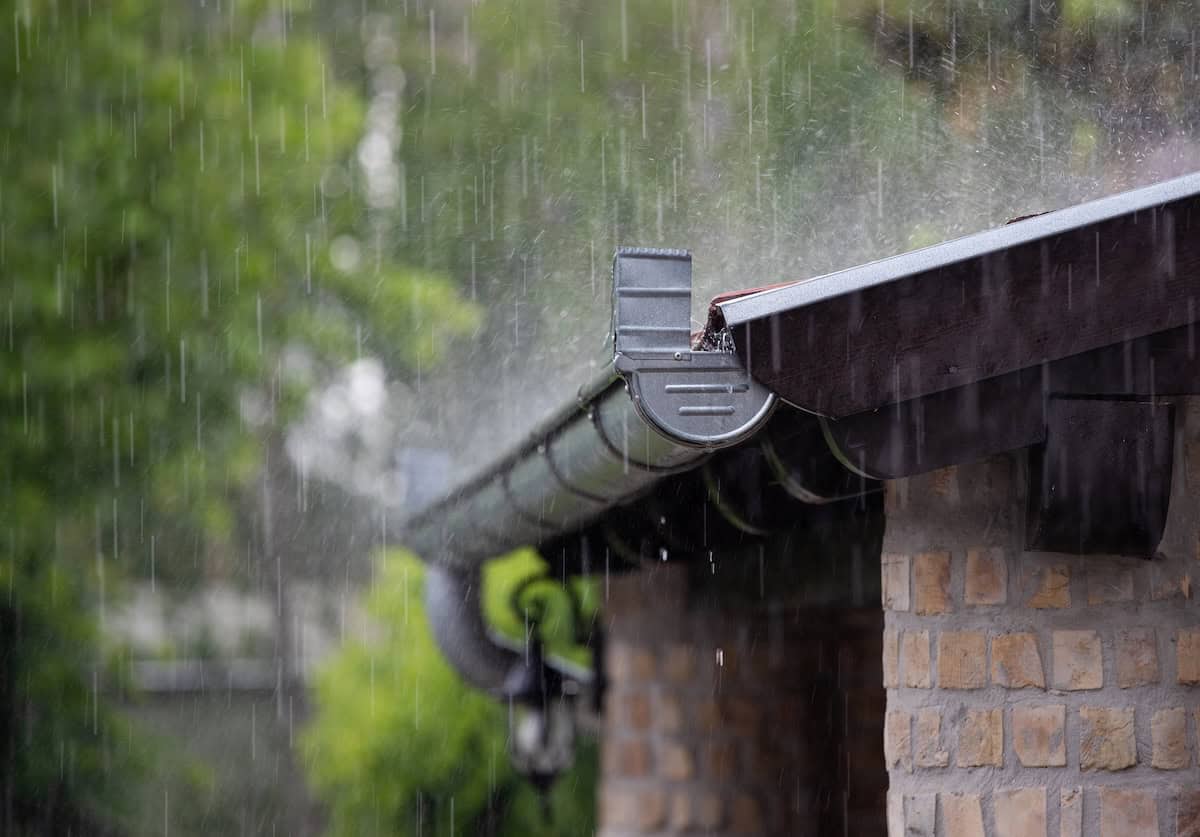 Heavy rain falling on the roof and metal gutter of brick house in summer season