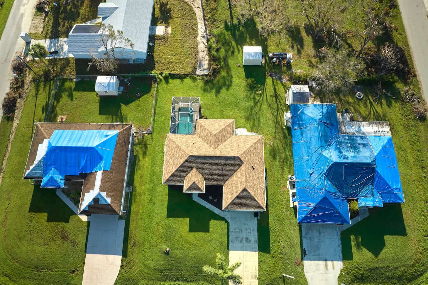 Top view of leaking house roof covered with protective tarp sheets against rain water leaks until replacement of asphalt shingles. Damage of building rooftop as aftermath of hurricane Ian in Florida.