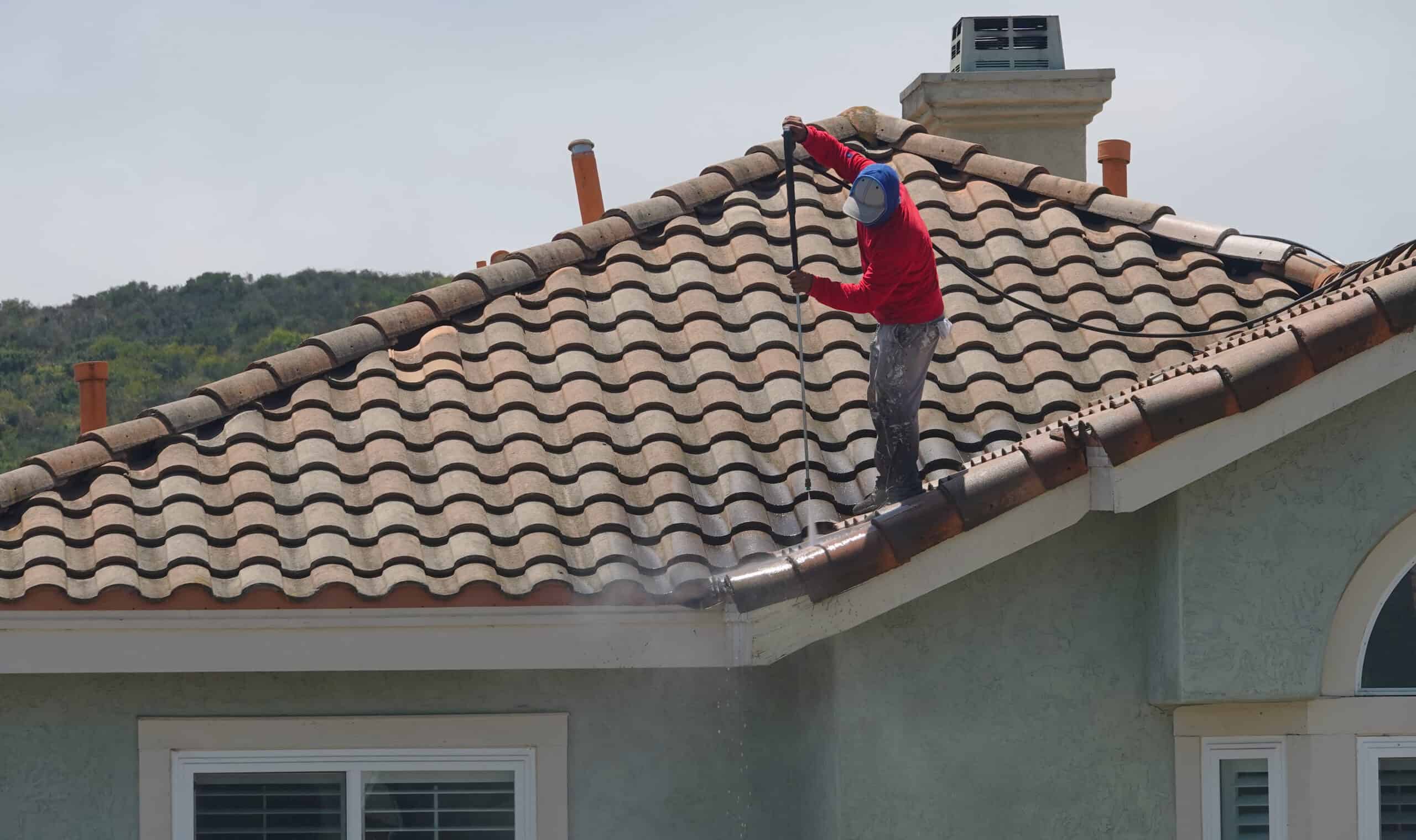 A worker pressure-washes the tile roof of a home