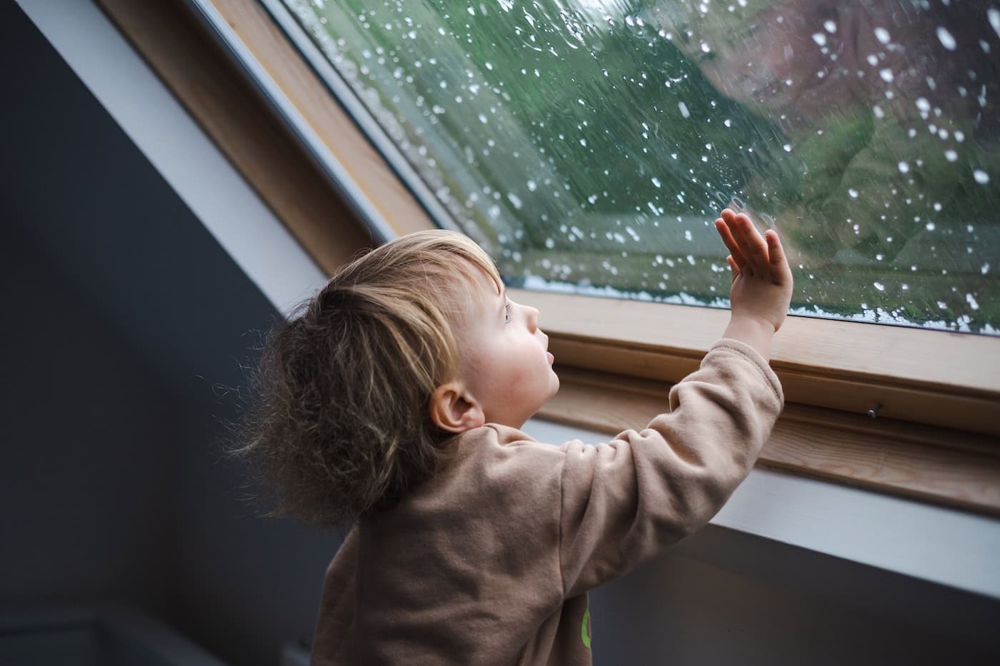 little boy looking at rain in skylight