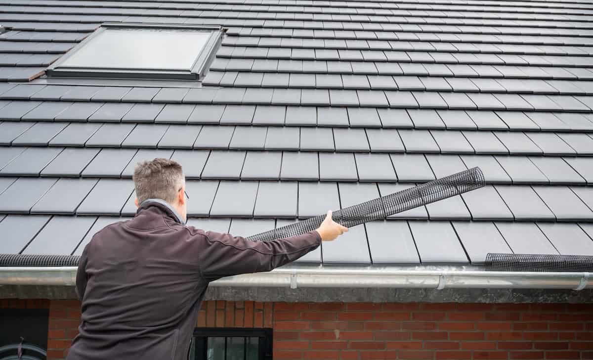 Man puts a gutter mesh to the rain gutter to protect the gutter from leaves.